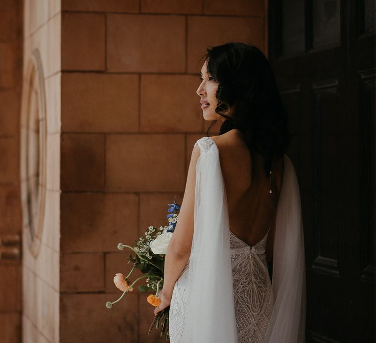 Bride wearing a plunge open back Eliza Jane Howell wedding dress with cape veil and bead details