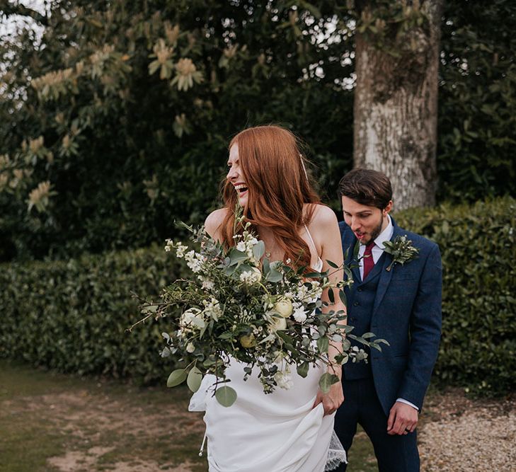 Beautiful bride in a satin slip wedding dress holding a giant green foliage and white flower wedding bouquet with roses and eucalyptus 