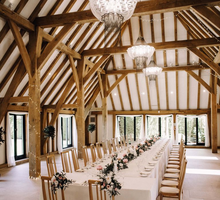 Exposed wooden beam venue Old Kent Barn with fairy lights and long banquet table