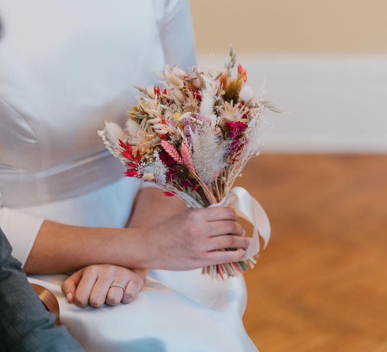 Bride holds small dried flower bouquet with vibrant colours tied with white silk ribbon