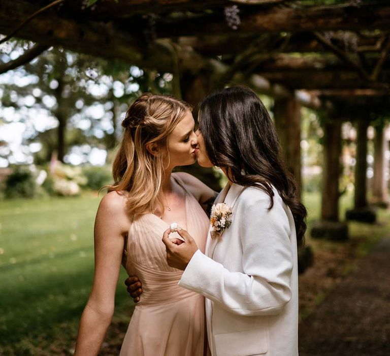 Brides kissing at their outdoor wedding reception under a pergola 