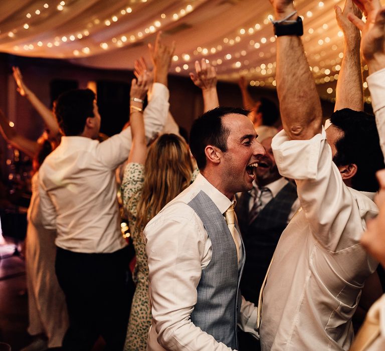 Groom in blue waistcoat and gold tie dances with wedding guests at evening wedding reception in Dorset