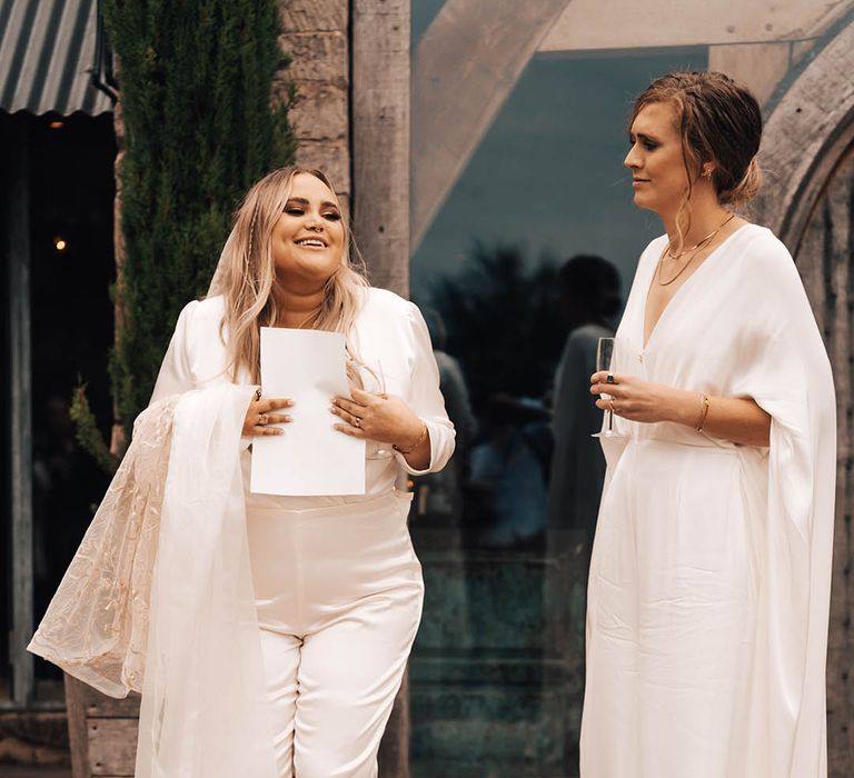 Brides stand together wearing white jumpsuits on their wedding day outdoors 