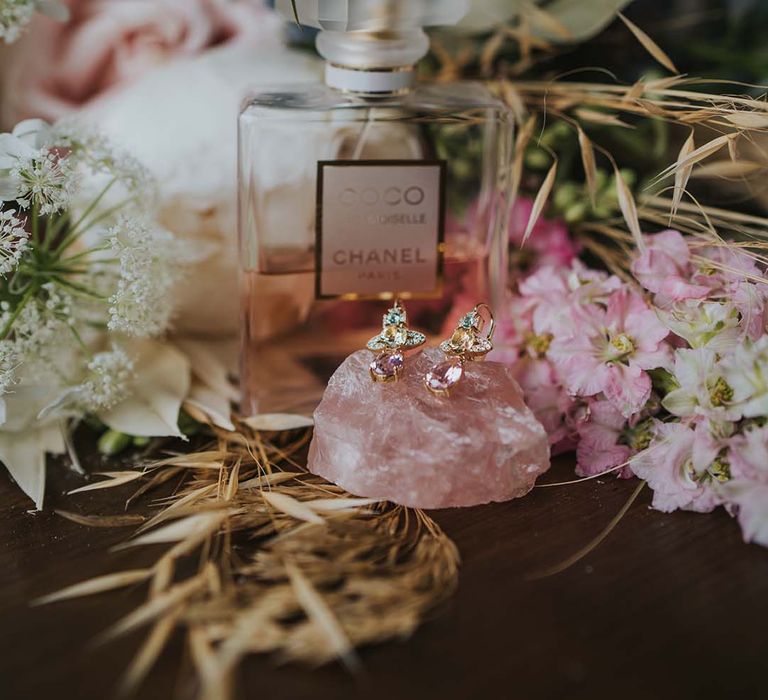 Coco Chanel perfume surrounded by florals in front of wedding rings set upon pink crystal 