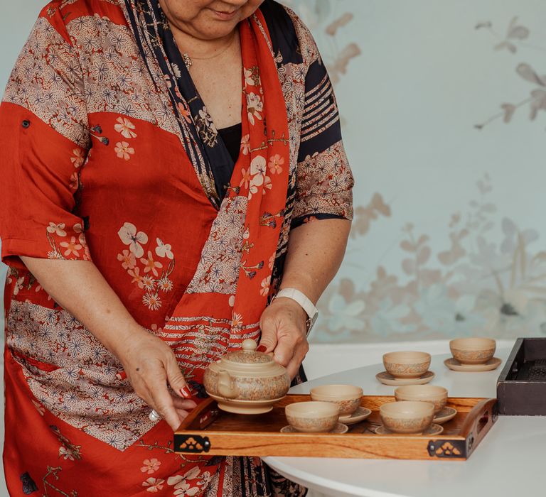 Woman in red, white and black silk patterned dress organised Chinese tea set for traditional Chinese tea wedding ceremony at Wasing Park wedding