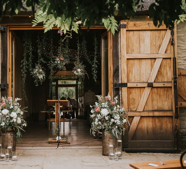 Barn doors at Tythe Barn with florals in milk churns, candle and hanging florals set up for wedding ceremony