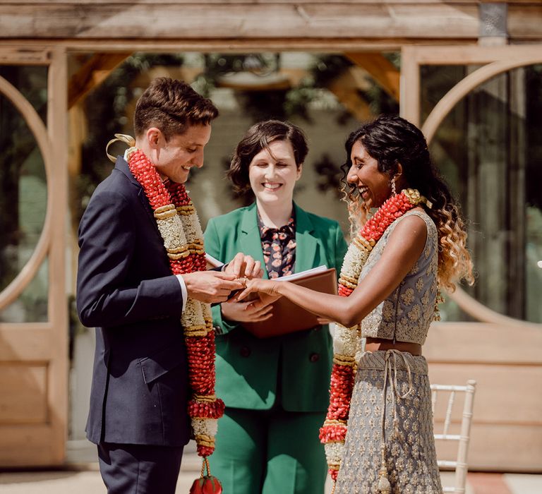 Outdoor celebrant interfaith led wedding ceremony with Indian bride in a gold sari and groom in a navy three-piece wedding suit 