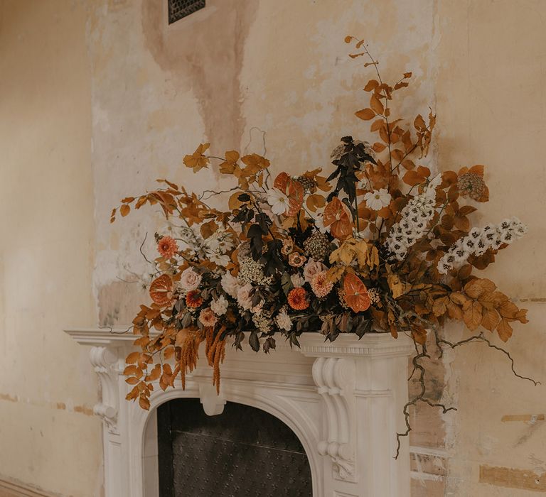 Orange and brown fireplace mantel wedding floral arrangement with branches, anthuriums, roses and dahlias