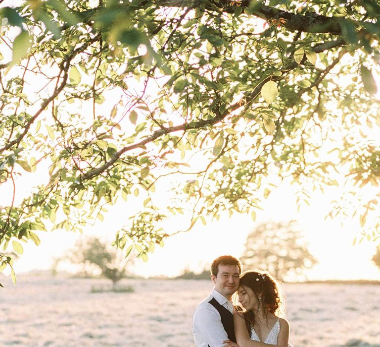 Groom wraps his arms around bride as they stand outdoors