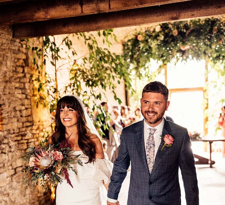 Bride & groom smile and hold hands as they walk with one another after their wedding ceremony