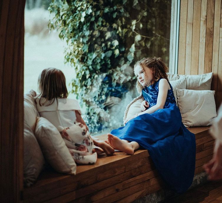 Little girl sits at the window wearing blue sequinned dress