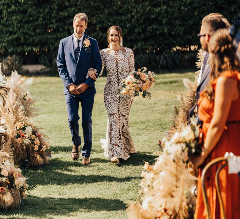 Bride in lace wedding dress walking in outdoor setting with father navy three piece suit 