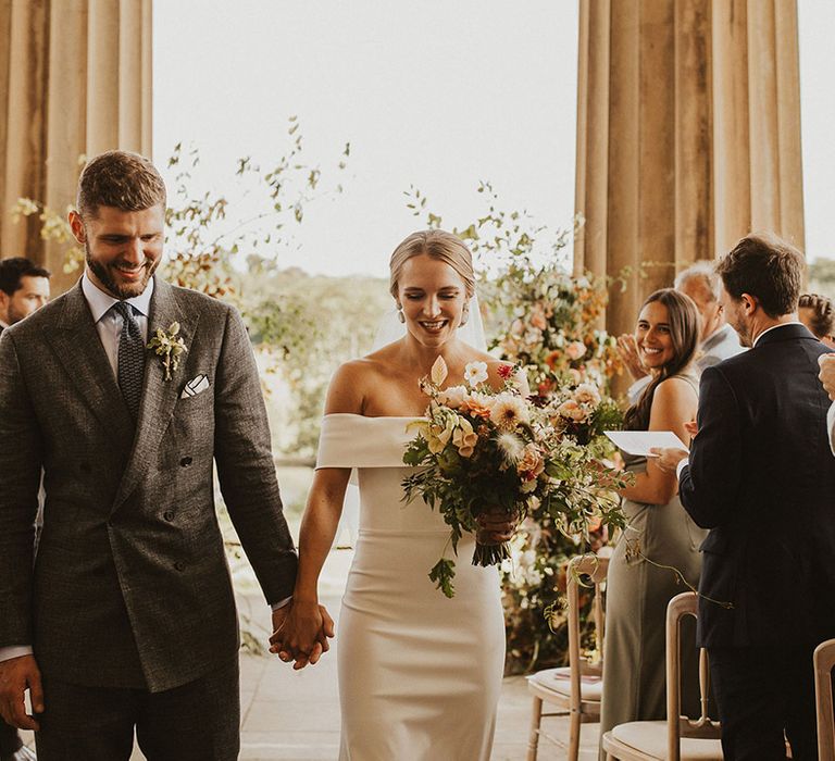 Bride & groom smile as they walk down the aisle holding hands on their wedding day