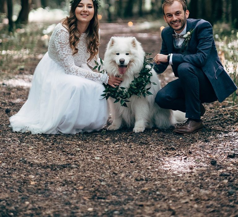 Bride & groom sit with their fluffy white dog who wears floral collar on their wedding day as ring bearer 