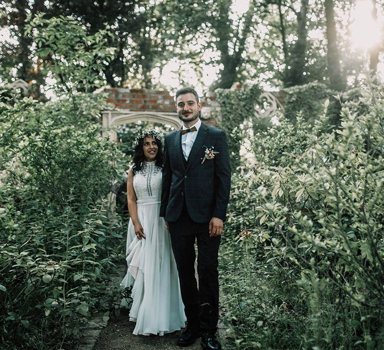 Bride & groom stand between trees and foliage on their wedding day