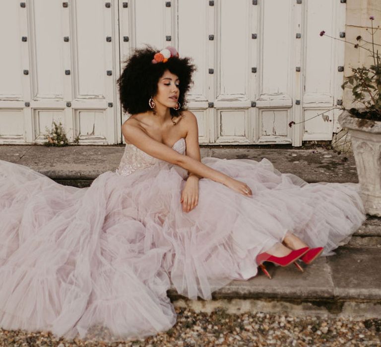 Black bride with afro hair wearing a pompom headpiece in a pink tulle skirt and red stiletto wedding shoes 