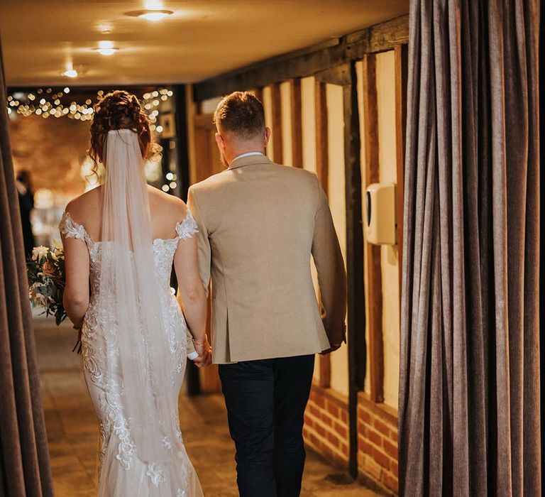 Bride with veil, lace off the shoulder wedding dress with train and groom in beige suit jacket