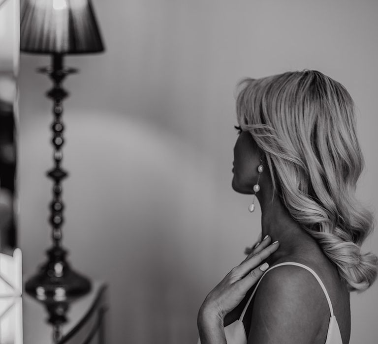 Bride with long wavy barrel curls and dangly pearl earrings on the wedding morning 