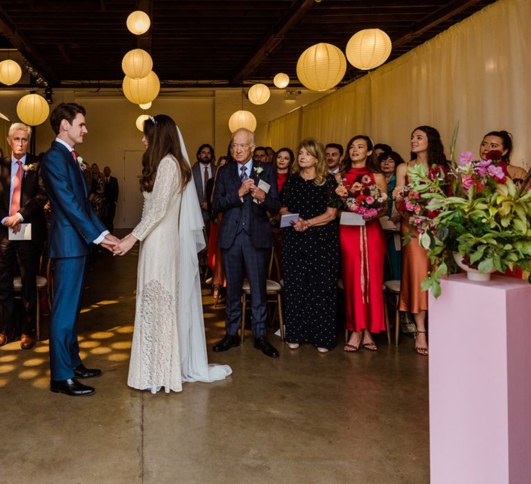 Wedding ceremony for couple at Trinity Buoy Wharf venue with hanging paper lanterns and pink pedestals for wedding flowers