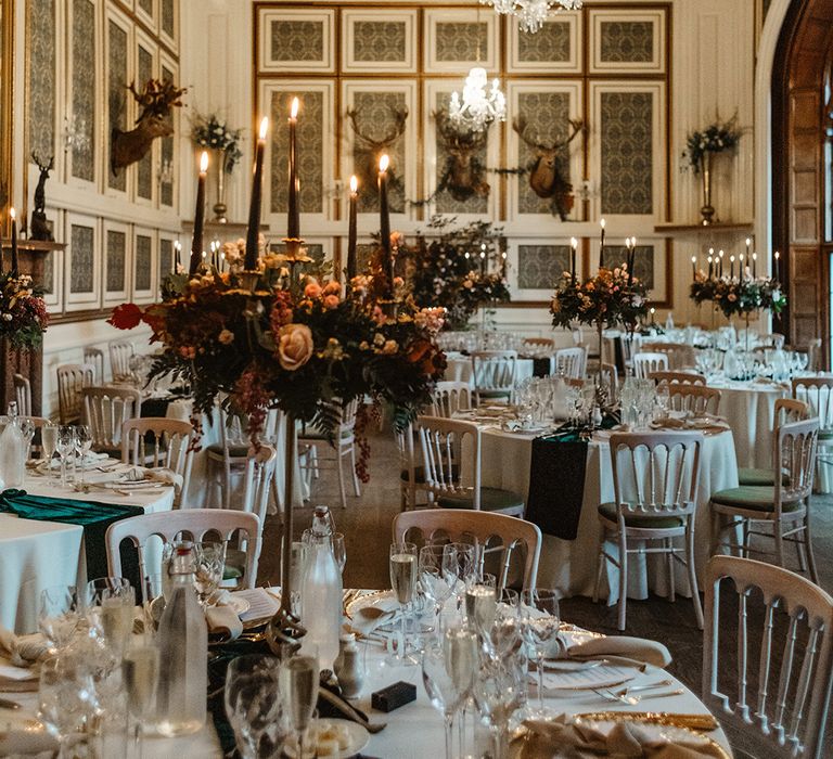 Table settings with black candles and rose wedding flower centrepieces with white napkins and plates and gold details 