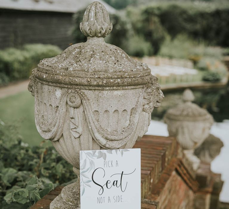 Wedding sign with leaf design and cursive font directing the guests to sit anywhere