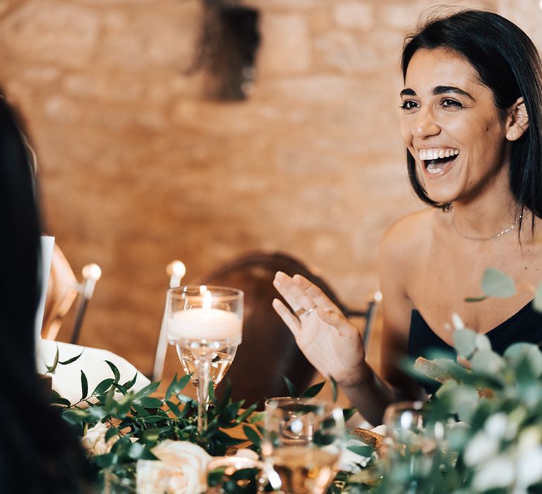 Wedding guest seated at the rustic styled tables wearing black laughs at the speeches