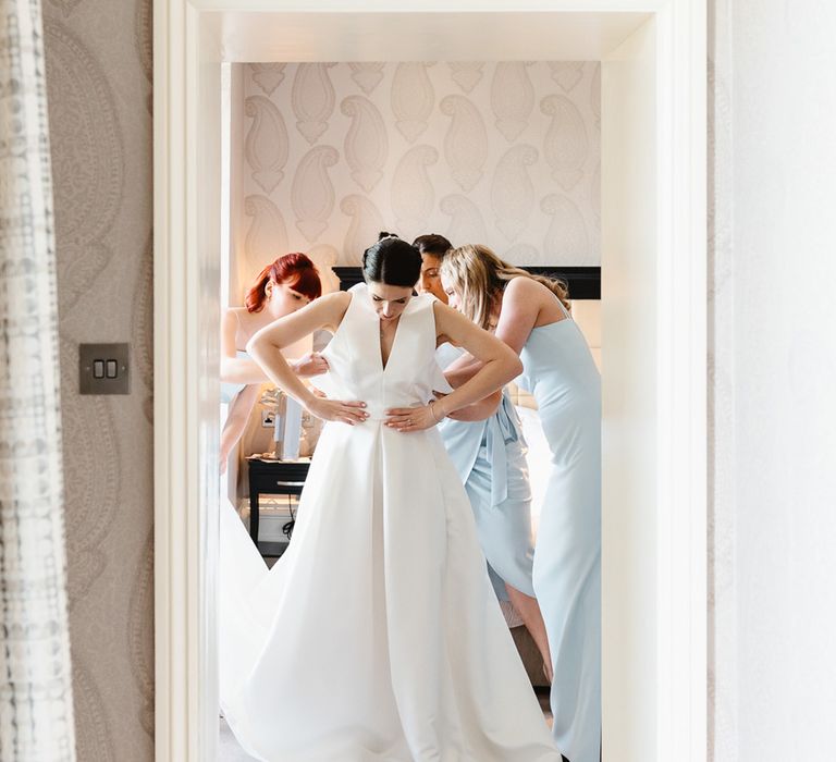 Bridesmaids in pale baby blue dresses help the bride into her halter neck Jesus Peiro wedding dress with bow