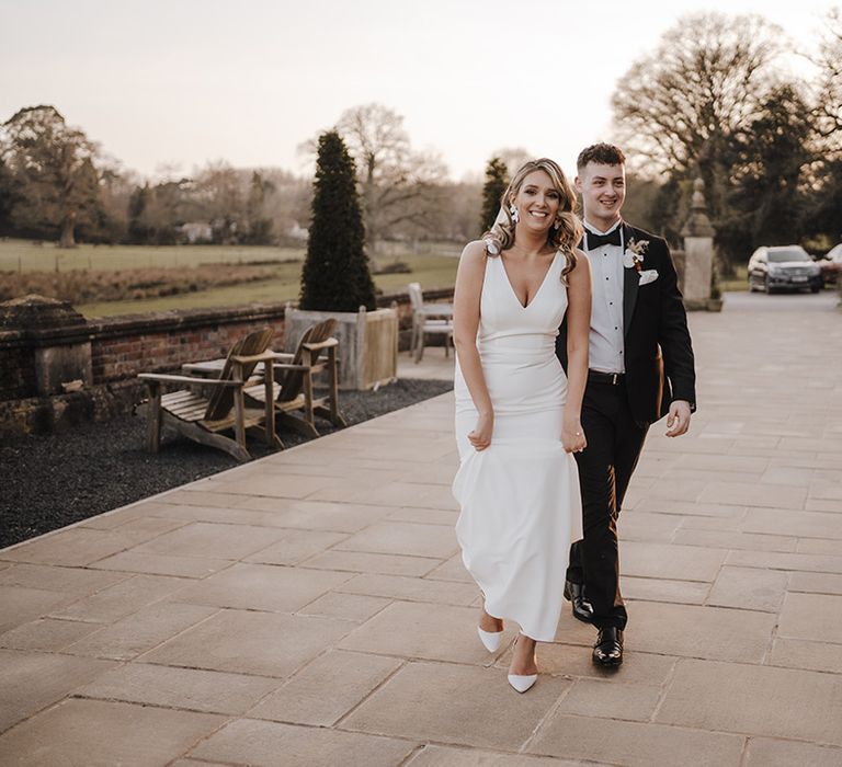 Bride in Made with Love v-neck wedding dress walks into wedding reception with groom in black tie 