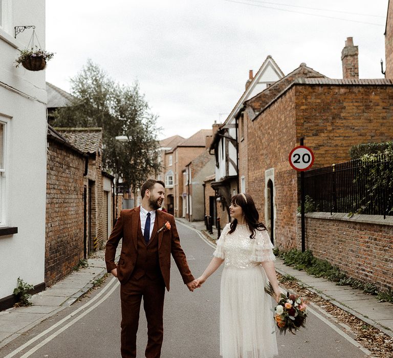 Bride and groom hold hands as they walk around together after their city wedding