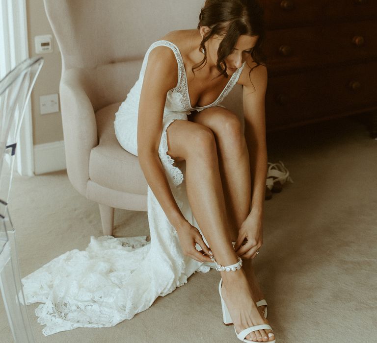 Bride in v-neck lace wedding dress with front slit puts on a pearl anklet for her wedding