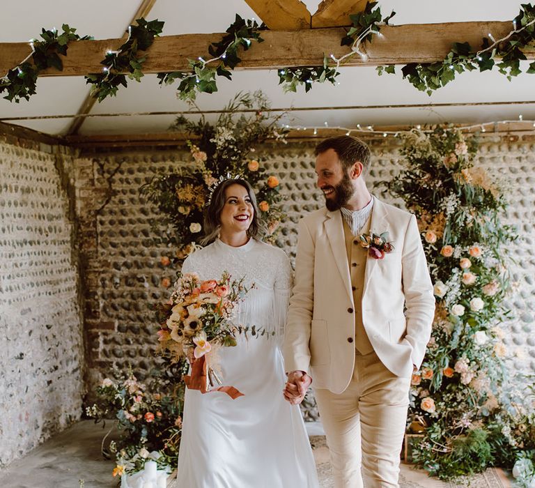 Groom in a beige suit holding hands with a bride in a satin tassel wedding dress at Montague Farm Hankham