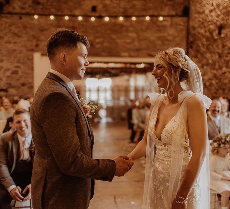 Bride in Elsie Made With Love wedding dress holding hands with groom at the altar with groom in brown three piece suit 