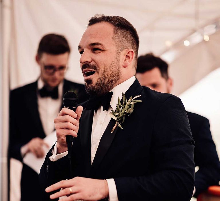 Best man in black tie reads out his speech wearing simple green foliage buttonhole 