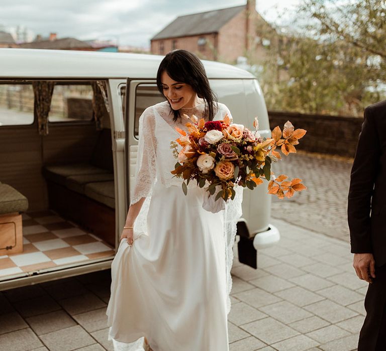 Bride leaves vintage VW camper van as she holds brightly coloured Autumnal style bouquet 