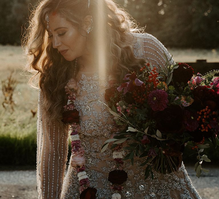 Bride holds brightly coloured floral bouquet on her wedding day as the sun begins to set behind her 