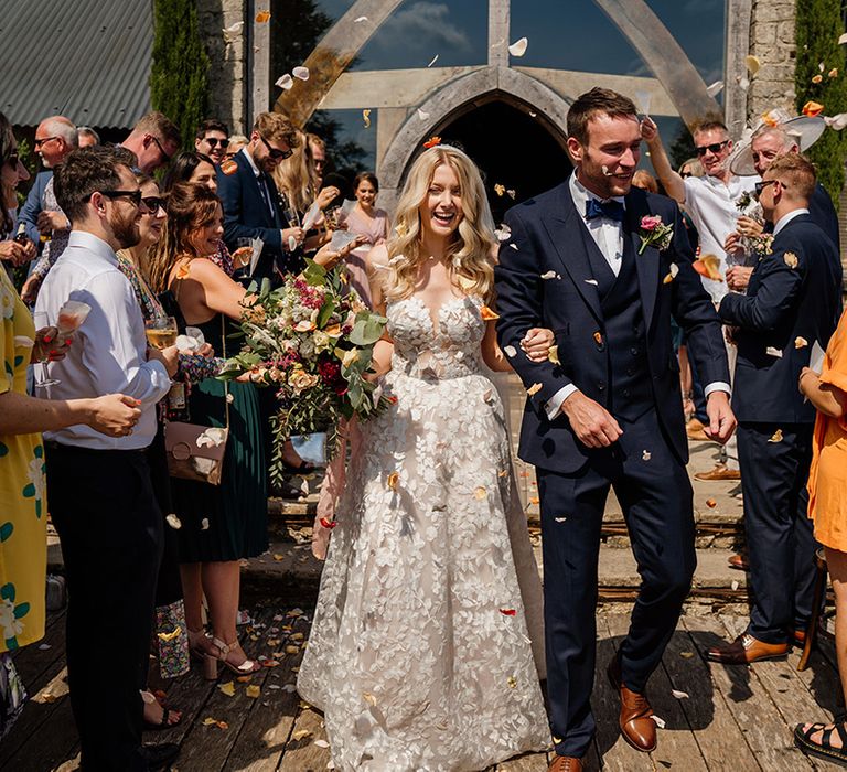 Groom in three piece blue suit with blue bow tie has confetti moment with bride in strapless lace Lillian West wedding dress