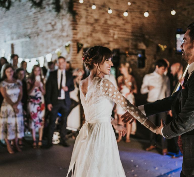 Bride in a long sleeve polka dot wedding dress being twirled on the dance floor at her rustic barn wedding 