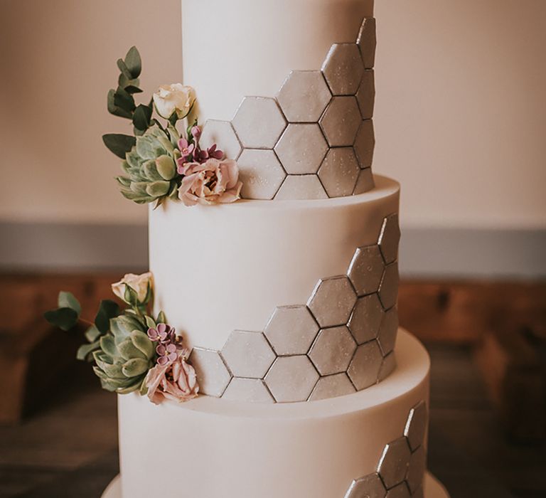 Three tier traditional white wedding cake with hexagonal detailing and flower decor 