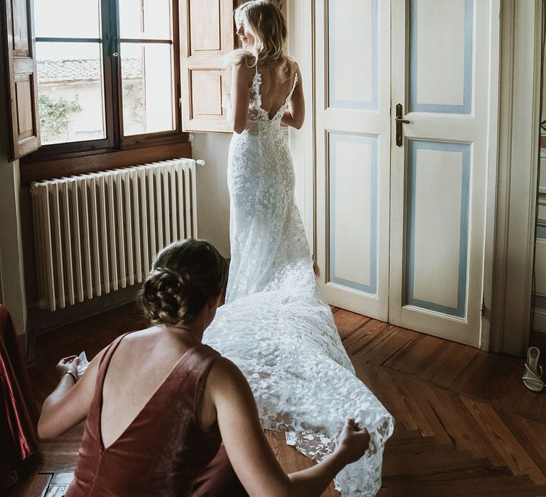 Bride wears lace V shaped back Emmy Mae Bridal wedding dress as her bridesmaid moves her train around her 