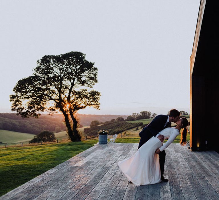 Groom leans the bride down for a kiss during sunset at The Barn at Botley Hill wedding venue 