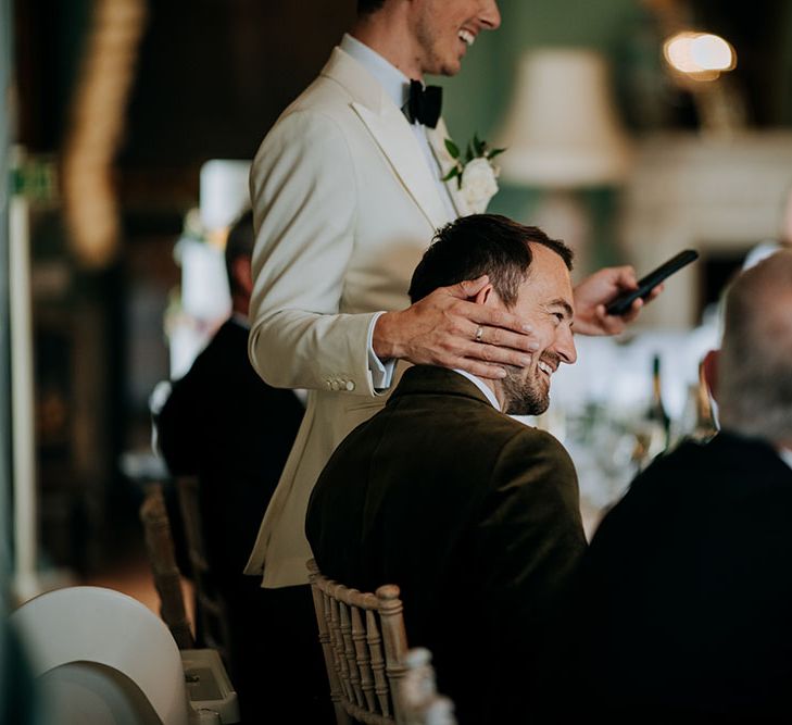 Groom rests his hand on his grooms head during wedding speeches 