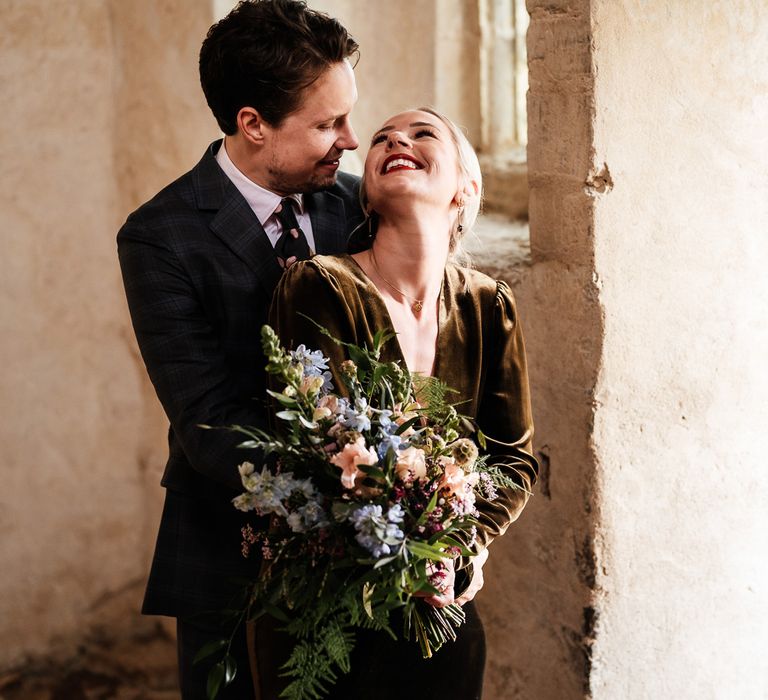 Bride holding pastel bridal bouquet looks back toward groom wearing tartan suit and floral tie for post ceremony couples portraits 