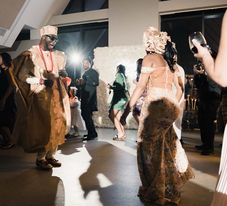 Groom wears sunglasses and dances with his bride, both wearing traditional Nigerian dress for evening reception 