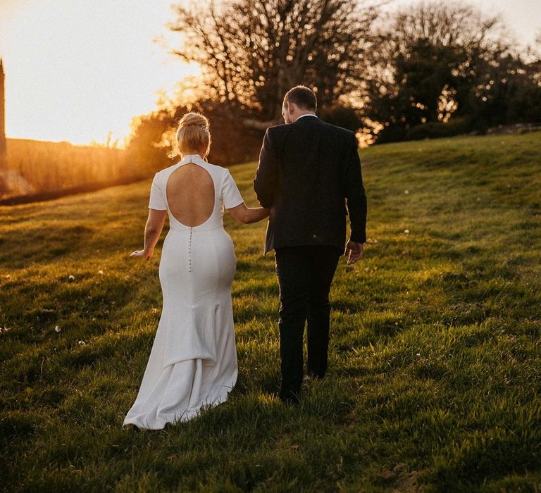 Bride and groom walk together as the sun sets 