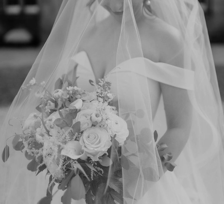 Bride carrying a white flower bouquet with an off the shoulder wedding dress and veil with pearl drop earrings 