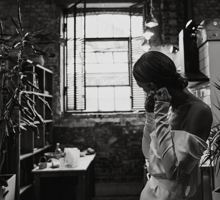 Bride with a sleek bun wedding hair puts in her earrings on her wedding day  