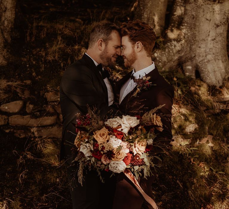 Grooms in black tie rest their foreheads against each other for a cute couple portrait 