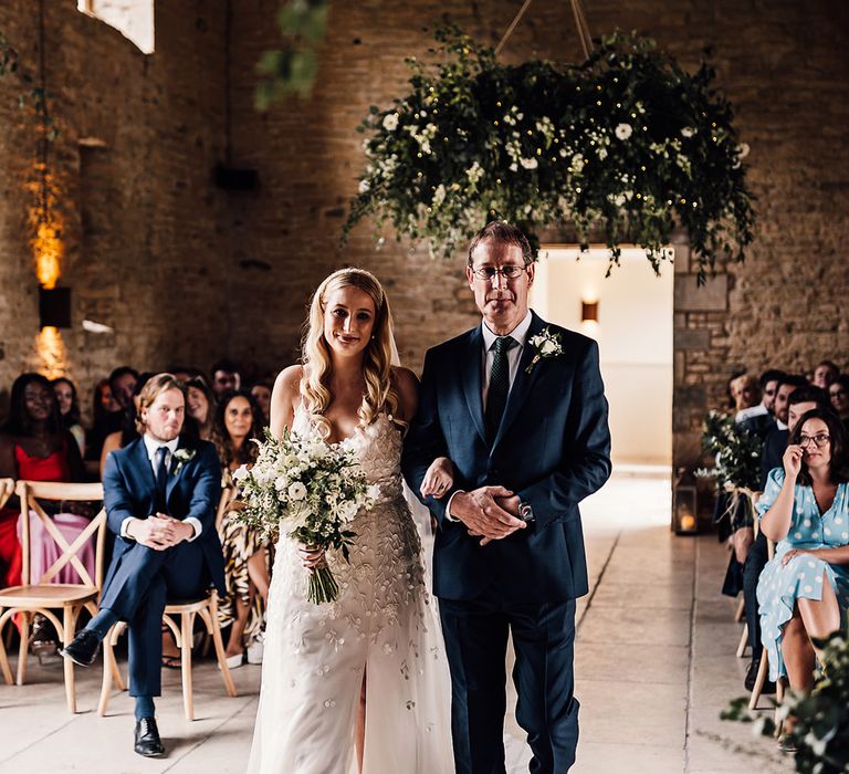 Father of the bride walks the bride in an applique wedding dress down the aisle 