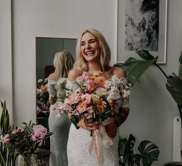 Bride in lace boho two piece smiling and laughing, holding colourful mixed floral bouquet 