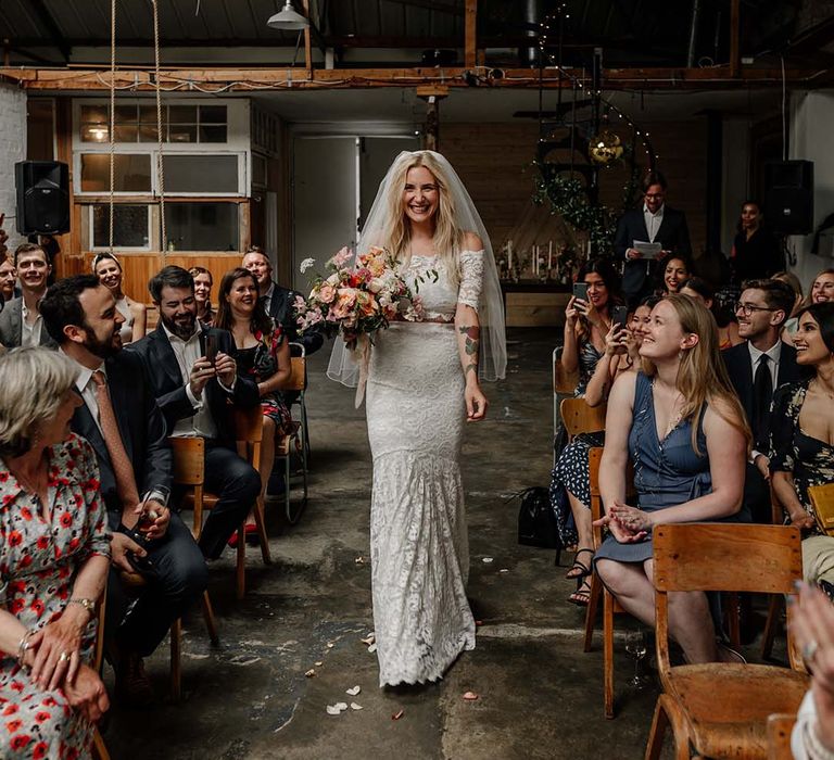 Bride in lace boho two piece, colourful mixed floral bouquet and short veil walking down the aisle at Hackney Studios